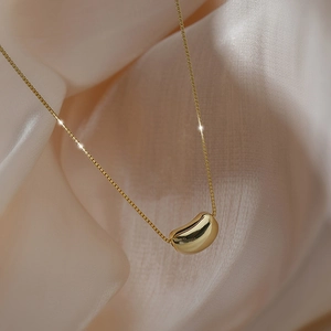 Elegant gold titanium steel necklace with a smooth bean pendant on beige silk background