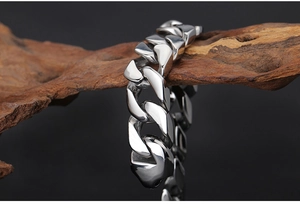Gros plan d'un bracelet gourmette argenté poli enroulé sur du bois brun rustique