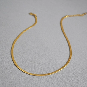 Detail of flat golden snake bone chain necklace on minimalist grey background
