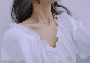 Close-up of a minimalist gold snake bone chain necklace worn by a model on plain background