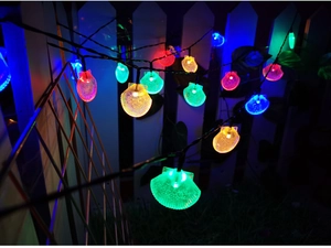 Close-up of multicolor shell LED fairy lights glowing on a garden fence at night