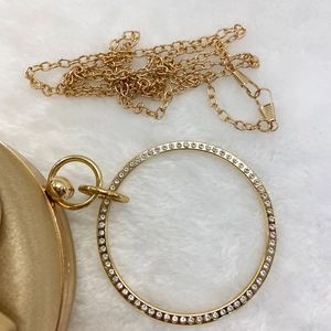 Detail of gold silk evening clutch bag with sparkling rhinestone ring handle and chain