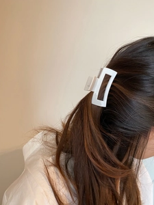 Detail of white rectangular hollow hair claw clip worn on model's dark hair