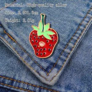 Detail of red strawberry enamel brooch with green leaves pinned on blue denim fabric