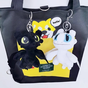 Plush black and white dragon keychains hanging as decorative charms on a black tote bag