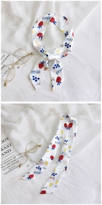 Detail of skinny silk scarf with fruit print tied on bag handle over white fabric