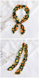 Detail of dark green silk scarf with orange print tied on a handbag handle for decoration