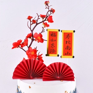 Detail of red plum blossom, paper fans, and golden scrolls for birthday cake decor