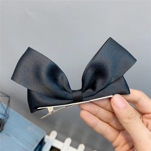 Close-up of large black satin bow hair clip with silver metal duckbill clip held by hand