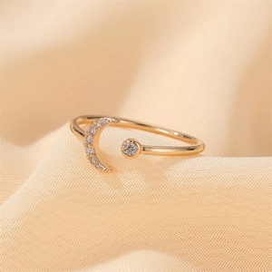 Macro detail of gold moon crescent open ring with sparkling zircon stones on soft beige fabric