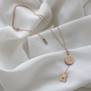 Detail of rose gold bear necklace with 18KGP engraving on a white fabric background