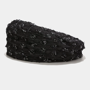 Detailed view of black and white tweed beret with textured weave and raw edge details