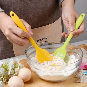 Silicone spatula set in yellow and green mixing batter in a glass bowl for baking