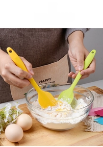 Detailed view of yellow and green silicone spatulas mixing batter in a glass bowl