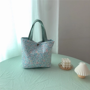 Close-up of floral bento bag with green handles and brown button closure detail