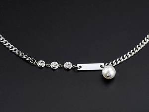 Close-up of silver necklace with three diamond studs, white pearl and rectangular tag