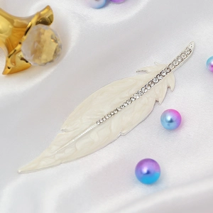 Exquisite cream feather brooch with sparkling rhinestones on elegant white silk background