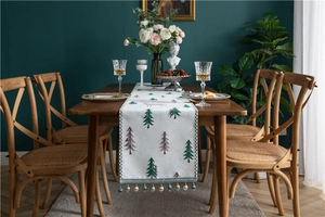 Detail of Christmas chenille table runner featuring reindeer patterns and tassel trim