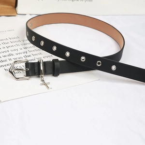 Détail de ceinture noire avec œillets argentés et un pendentif croix minimaliste suspendu