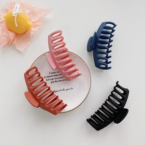 Close-up of four matte-textured large shark hair clips in pink, navy, red, and black colors