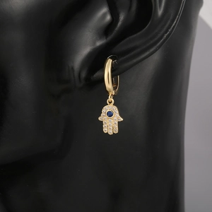 Macro detail of a golden Hamsa hand earring featuring white zircons and a blue gemstone