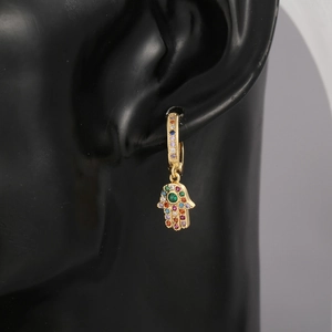 Close-up of gold Hamsa Hand earrings with colorful crystals and a central green stone
