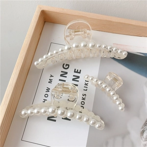 Close-up of elegant clear acrylic hair claw clips with white pearl accents on paper