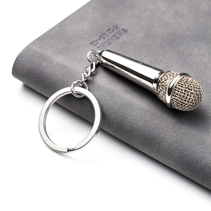 Polished silver metal microphone keychain on a gray leather notebook, creative gift accessory