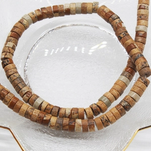 Macro detail of 6x3mm natural stone abacus beads in a gold-rimmed glass dish