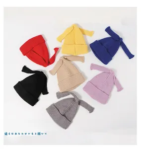 Flat lay of colorful knitted baby beanies with long bow accents in seven vibrant colors