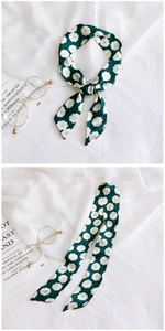 Detail view of a long green silk scarf with white floral patterns tied on a handle