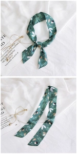 Detail of floral forest print silk twilly scarf tied in a bow on a white textured background