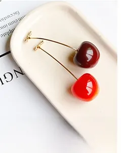 Detail of high-gloss cherry earrings in dark and bright red on a ceramic tray