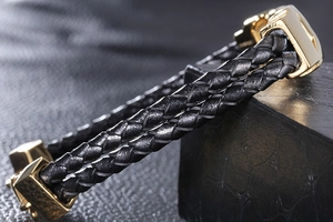 Close-up of double-layer black braided leather bracelet with polished gold metal buckle