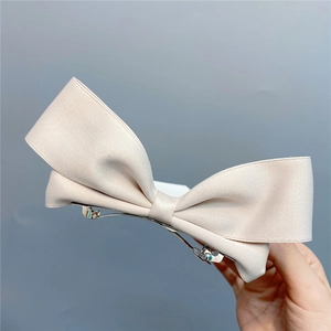 Close-up of a large beige satin ribbon bow hair clip with a metal spring fastener