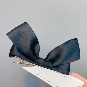 Detail of a black ribbon bow hair clip with silver alligator clip on a display card