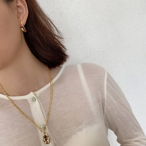 Detail of elegant gold U-shaped earring and textured pendant necklace set on a model