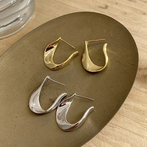 Detailed view of polished gold and silver U-shaped twisted earrings on a vintage tray