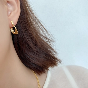 Macro shot of minimalist gold twisted geometric earring worn on ear showing glossy finish