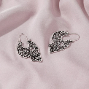 Close-up of gothic silver skull earrings with intricate hollow carved floral patterns