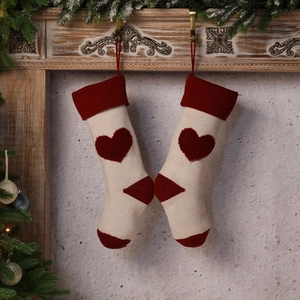 Knitted Christmas stockings with red heart pattern hanging on a rustic wooden fireplace