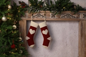 Close-up of red knitted Christmas stockings with 3D heart patterns hanging on a fireplace