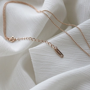 Detailed close-up of 18KGP rose gold beaded chain necklace on white fabric background