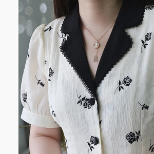 Rose gold bear coin necklace with white shell inlay, worn on a floral printed collar dress