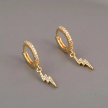 Detailed view of gold lightning bolt earrings with pavé cubic zirconia on grey surface