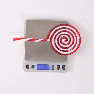Close-up of red and white spiral Christmas candy ornament being weighed on a scale