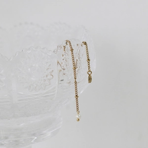 Close-up of a 18K gold plated titanium bracelet with tiny pearls on a glass rim