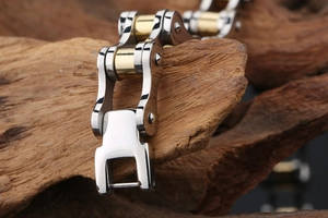Detail of gold and silver steel bike chain bracelet on a dark wooden textured display