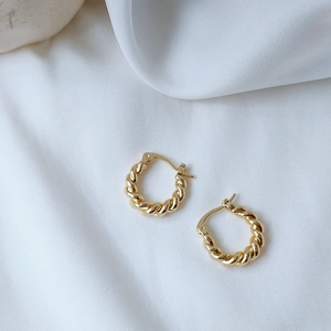 Detail of twisted 14K gold plated hoop earrings on elegant white silk background