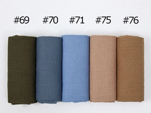 Detailed top view of large crinkled cotton scarves in diverse solid colors with frayed edges